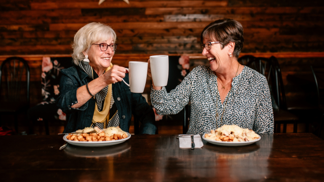 two ladies clinking coffee mugs