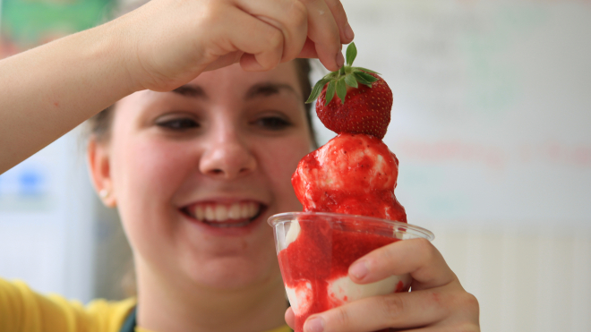 young girl holding a vanilla ice cream cone with strawberry sauce and a strawberry on top 