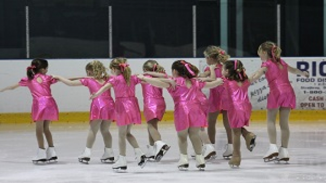 a group of young girls figure skating in pink outfits