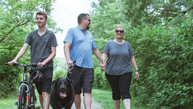 family of three and dog walking through a park 