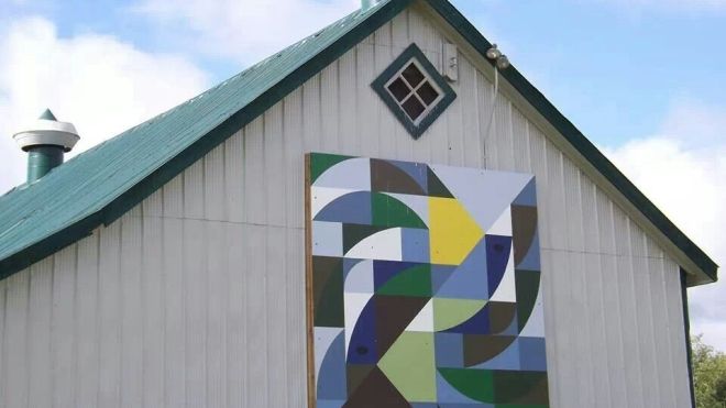 A green and white barn adorned with a kaleidoscope quilt-style mural. 