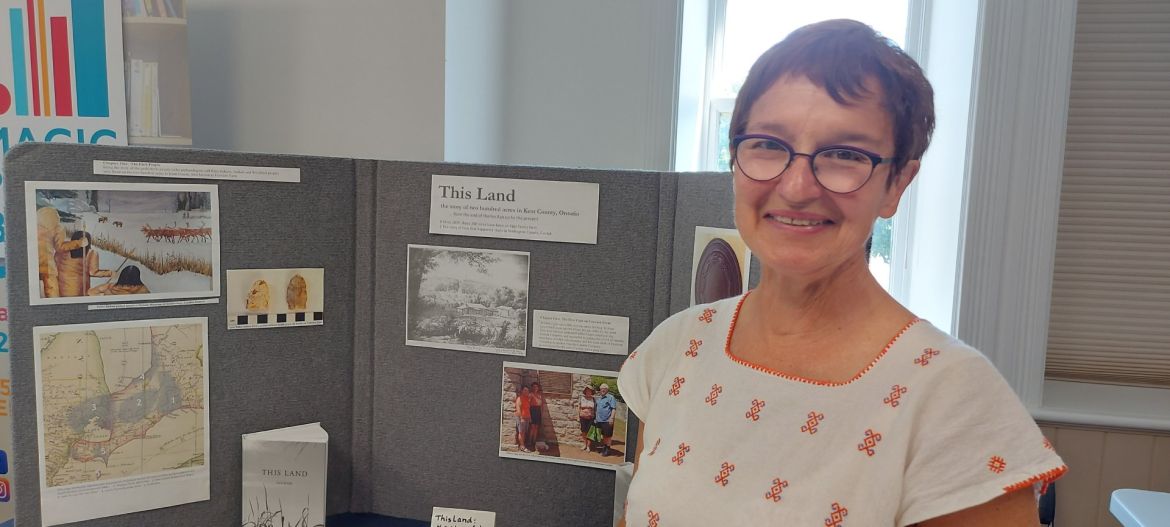 Woman standing beside a display about the book This Land and the history of food and agriculture in Southwestern Ontario.