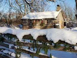 Fanshawe pioneer village picture of a log cabin covered in show with Christmas decorations hanging outside in the daylight