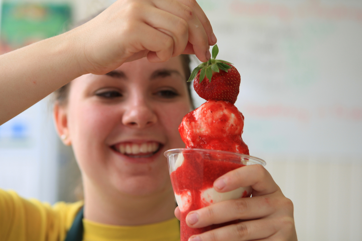 young girl holding a vanilla ice cream cone with strawberry sauce and a strawberry on top