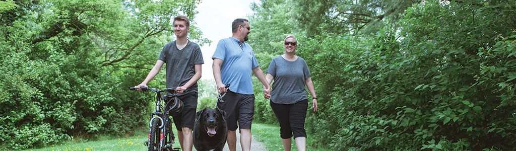 family of three and dog walking through a park 