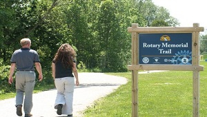 rotary trail with two passengers walking on a side walk/trail with the rotary memorial park sign beside them