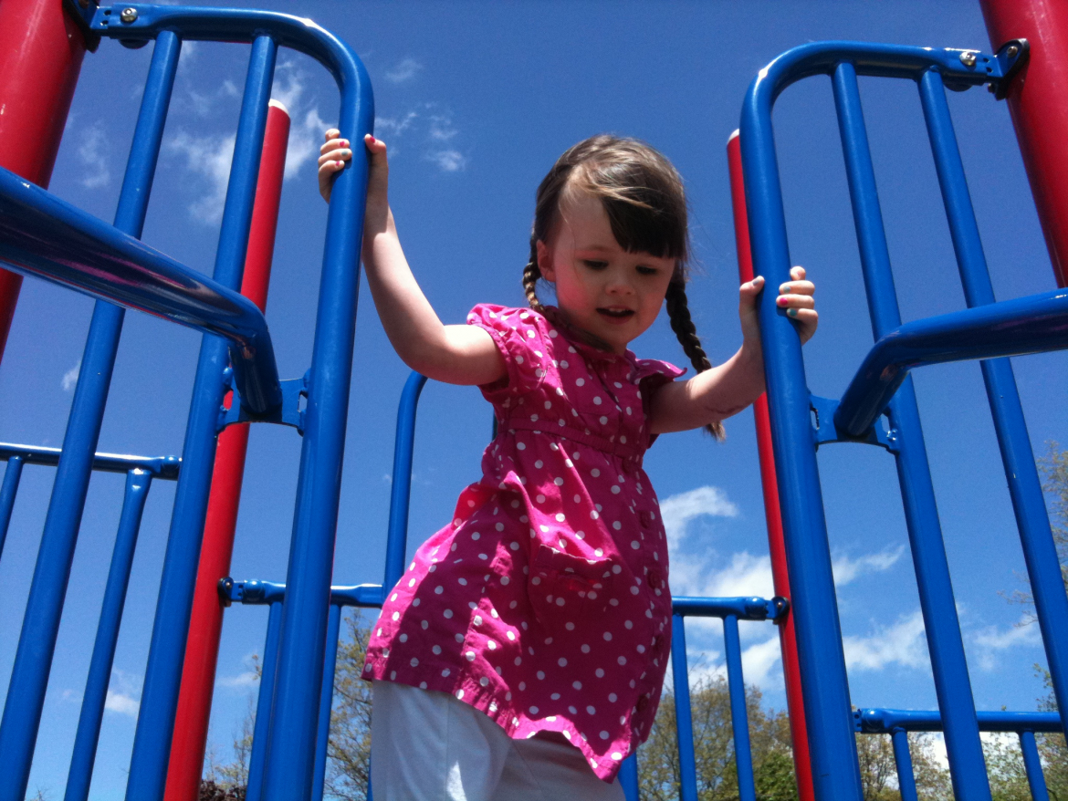 little girl playing on a playground  wearing a pink dress with white and two pig tail braids.